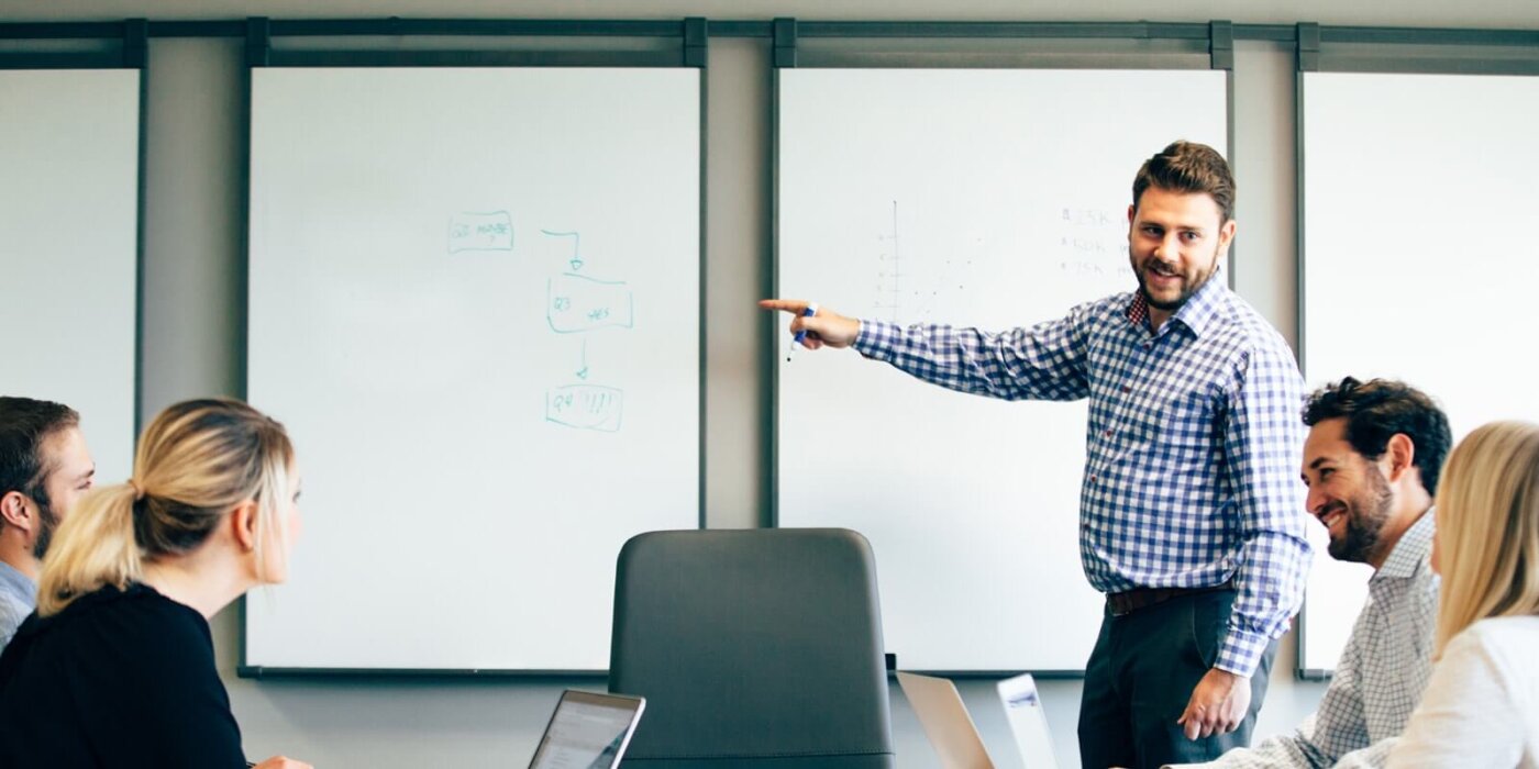 Team members having a meeting with the presenter at a whiteboard