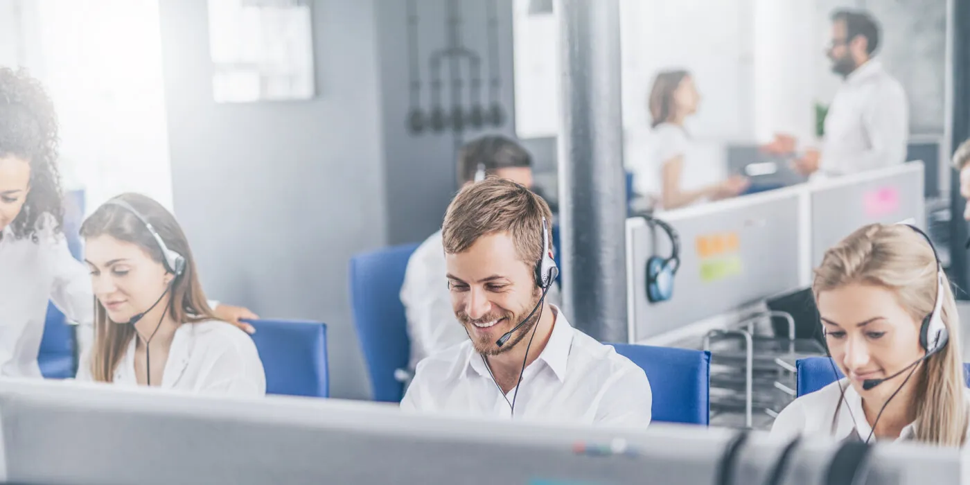 Call center worker accompanied by his team. Smiling customer support operator at work. Young employee working with a headset.