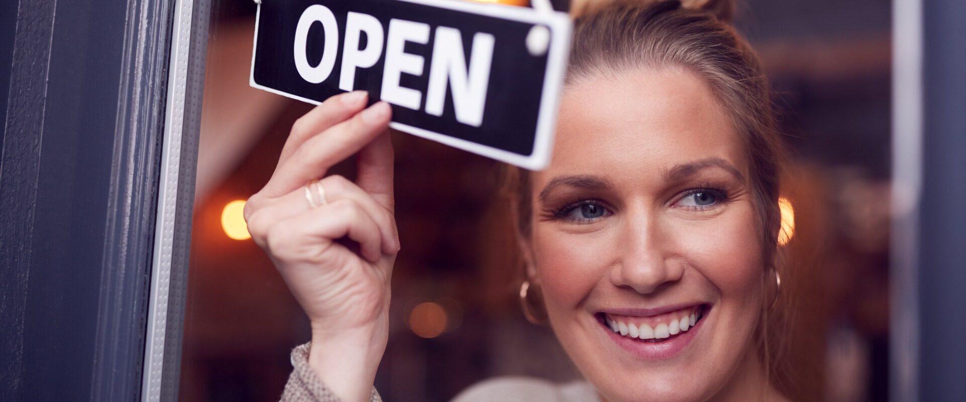 Female owner of a small-business turning around an open sign on a shop door.