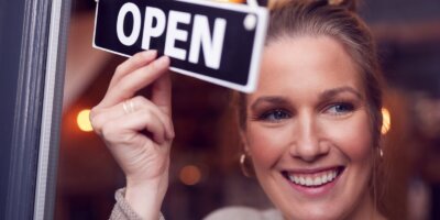 female owner of small business turning round open sign on shop door