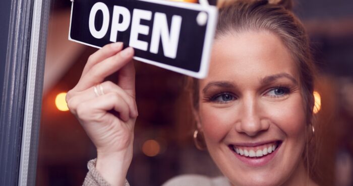 female owner of small business turning round open sign on shop door