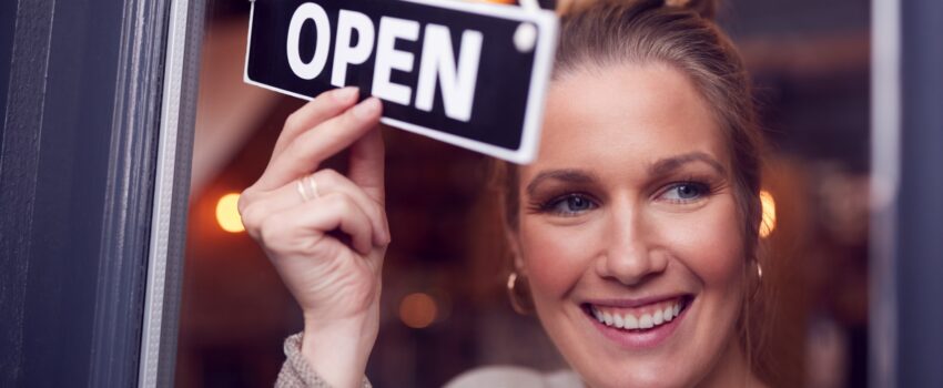 female owner of small business turning round open sign on shop door