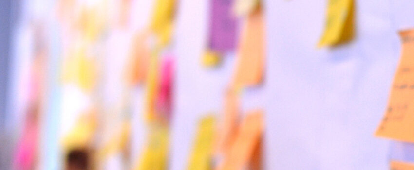 Header image of a slightly out-of-focus man updating a kanban board full of sticky notes.