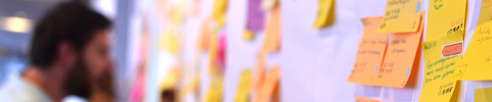 Header image of a slightly out-of-focus man updating a kanban board full of sticky notes.