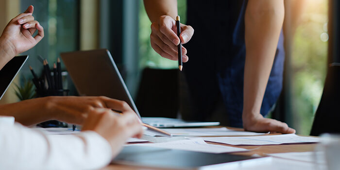 A team meets around a conference table filled with laptops and papers to plan their next digital solutions.