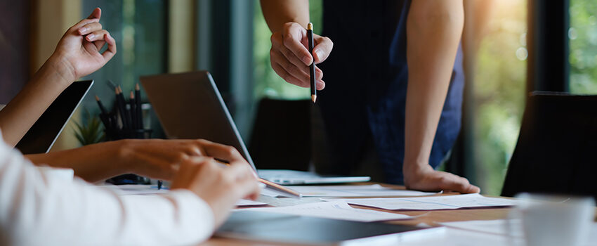 A team meets around a conference table filled with laptops and papers to plan their next digital solutions.