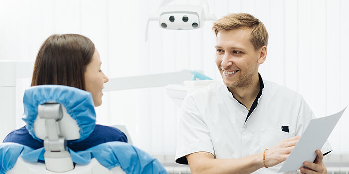A male dentist smiles as he consults with a patient.