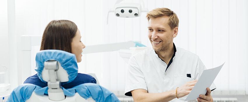 A male dentist smiles as he consults with a patient.