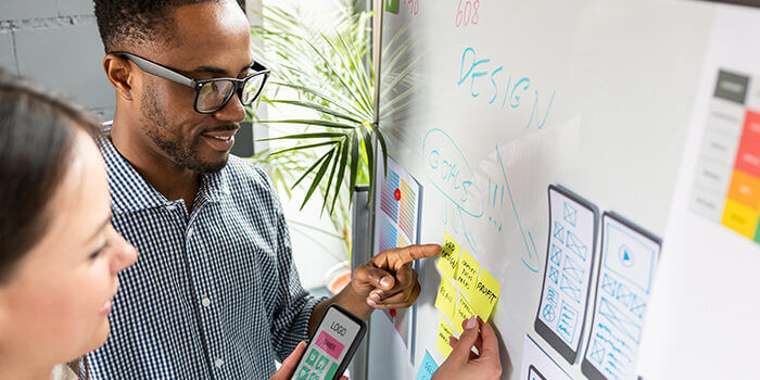 Two designers review their app design goals and mockup on a whiteboard.