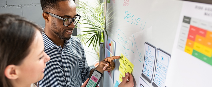 Two designers review their app design goals and mockup on a whiteboard.