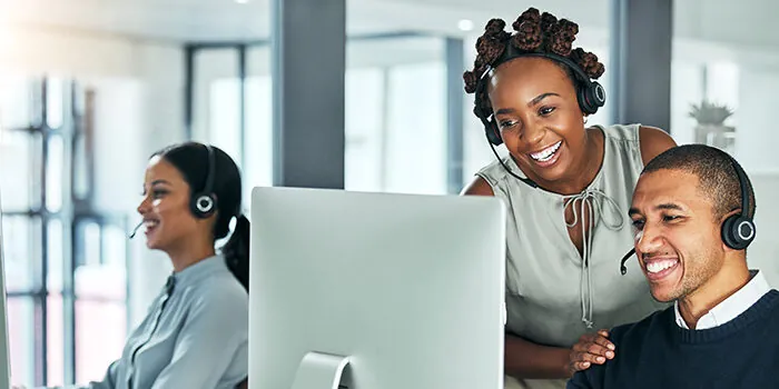 A call center manager shows a customer care agent how to do something on the computer.