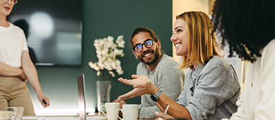 A woman smiles as she offers a suggestion to her project team gathered around a conference table.