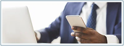 A man looks at his phone while his laptop is open right beside him.