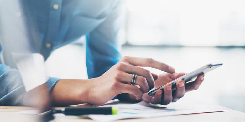 Person using a smartphone, wearing a blue shirt, seated at a desk