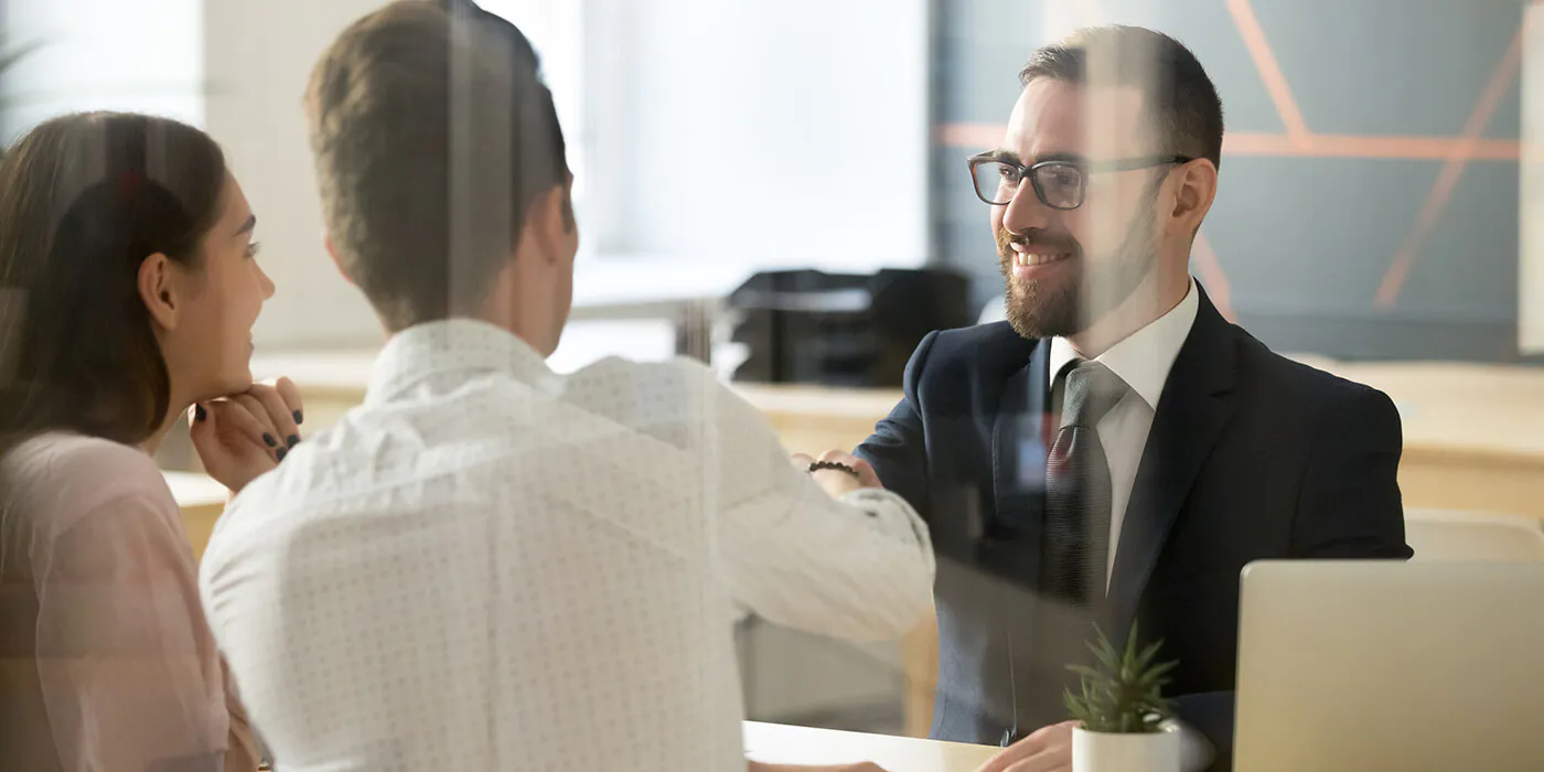 A banker shakes hands with a couple over his desk