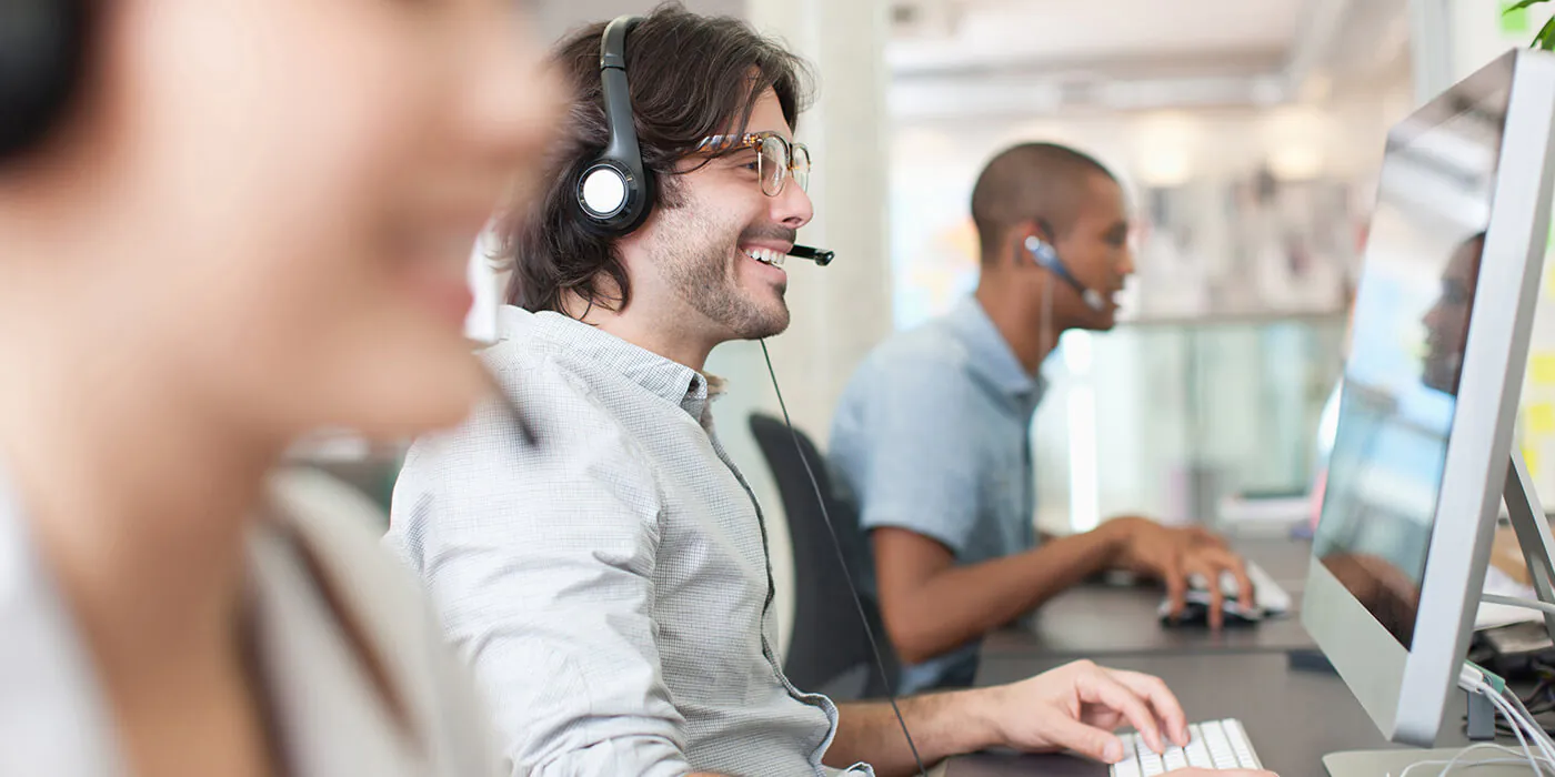 Customer service agents in headsets smile as they work on their computers